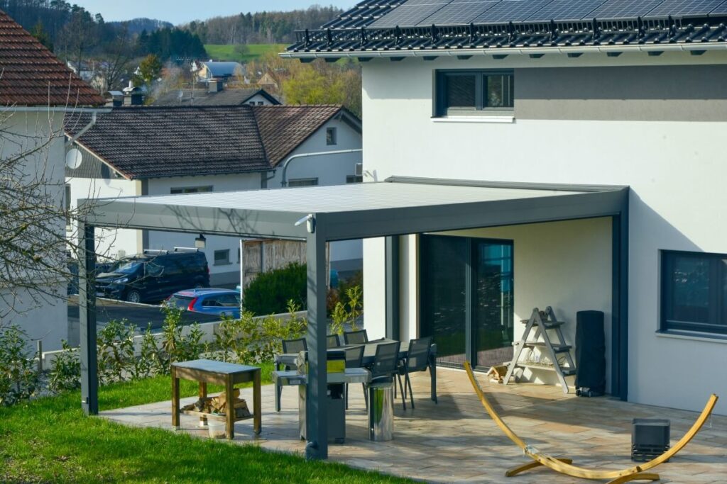 Przy nowoczesnym domu, na tarasie widać pergole lamelowe.