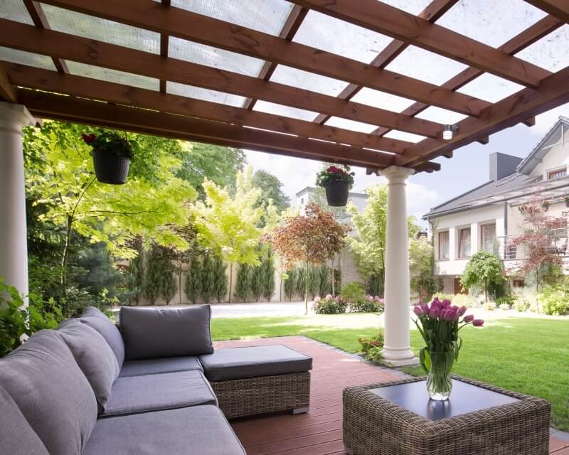 Na tarasie w ogrodzie znajduje się stylowy zestaw wypoczynkowy pod pergolą drewnianą.