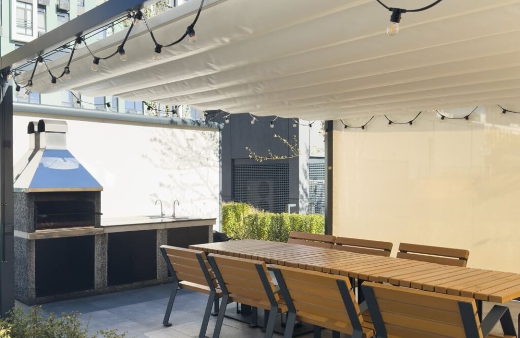 Przy tarasie z drewnianymi żaluzjami tarasowymi z ruchomym mechanizmem znajduje się stół i grill.